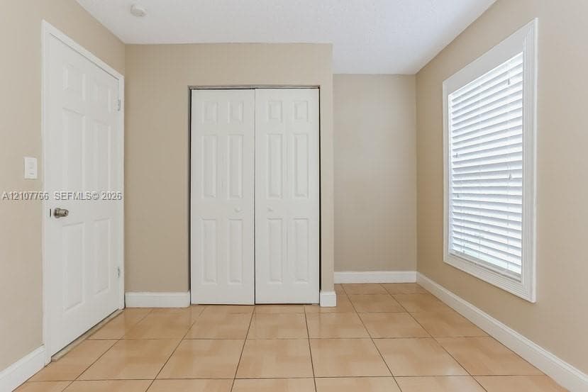 Neutral wall tones, ceramic tile flooring, a window with horizontal blinds, and two paneled interior doors