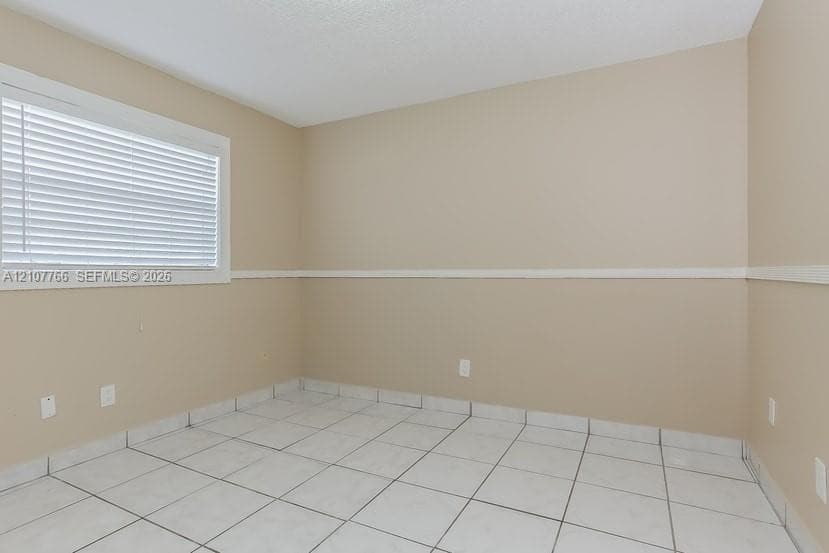 Neutral-toned walls featuring a horizontal chair rail, white tiled flooring, and a single window with fitted horizontal blinds