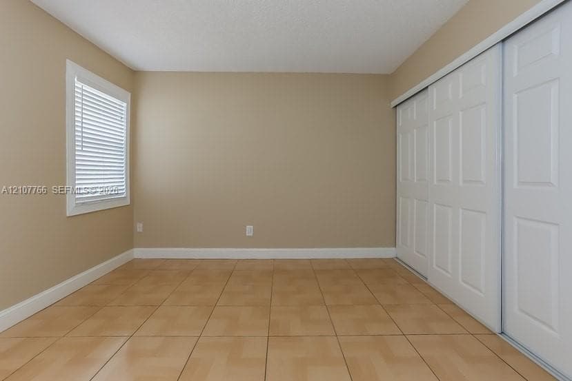 Room featuring tile flooring, neutral wall tones, a single-pane window with white slatted blinds, and a large sliding closet with white paneled doors