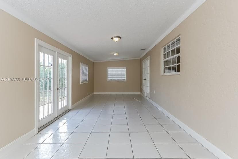 Interior room featuring large-format tile flooring, double glass-pane French doors, multiple multi-pane windows, and dual ceiling-mounted flush light fixtures