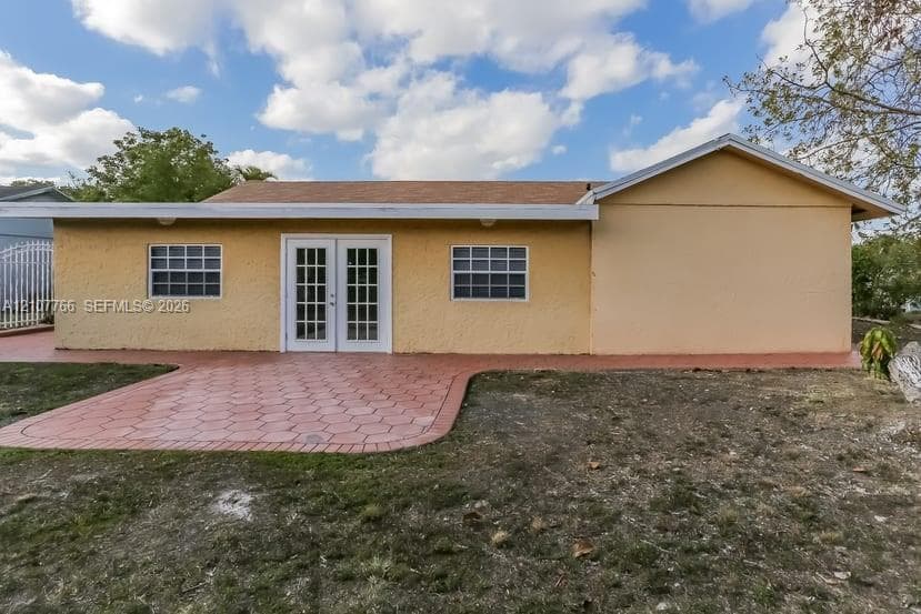 Stucco exterior featuring dual-paned grid windows, French doors, and patterned concrete patio surfacing