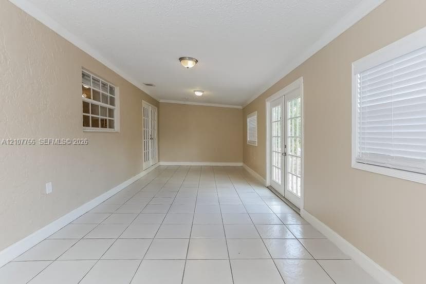 Large room featuring ceramic tile flooring, neutral wall paint, two sets of French doors, and windows equipped with horizontal blinds