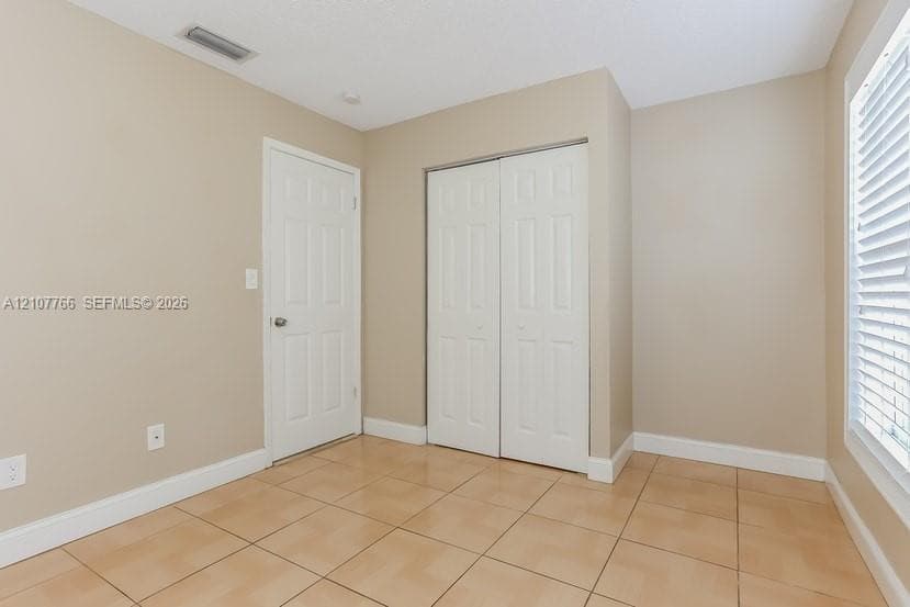 Neutral-toned interior featuring ceramic tile flooring, a dual-panel closet with white doors, a single-panel interior door, and a window with white horizontal blinds