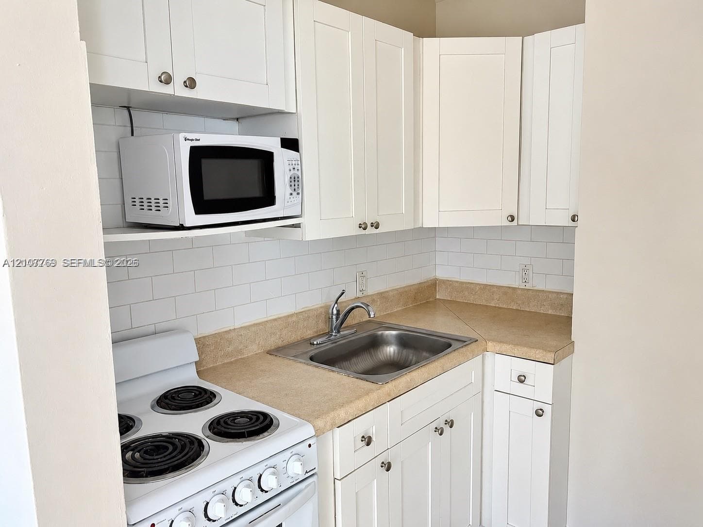 White shaker-style cabinetry, white subway tile backsplash, solid surface countertops, stainless steel drop-in sink, and white electric range