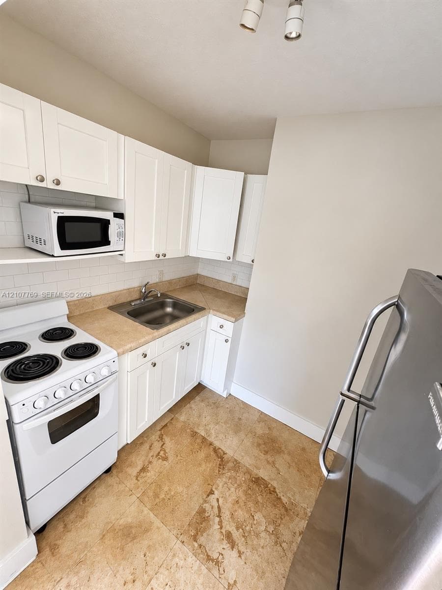 Kitchen featuring white cabinetry, stone-finish countertops, subway tile backsplash, stainless steel sink, and natural stone flooring