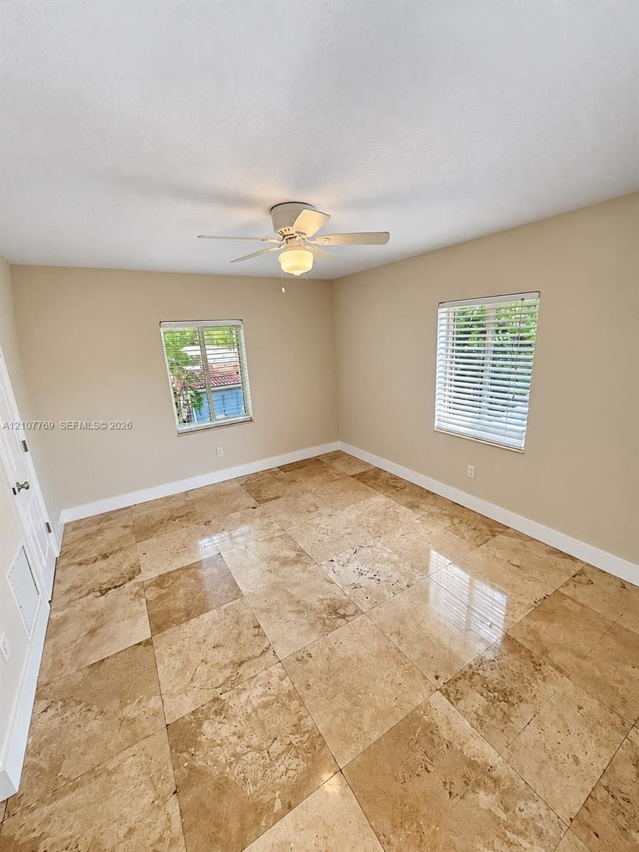 Neutral-toned interior space featuring polished stone tile flooring, dual windows with integrated horizontal blinds, and a centrally mounted ceiling fan with a light fixture