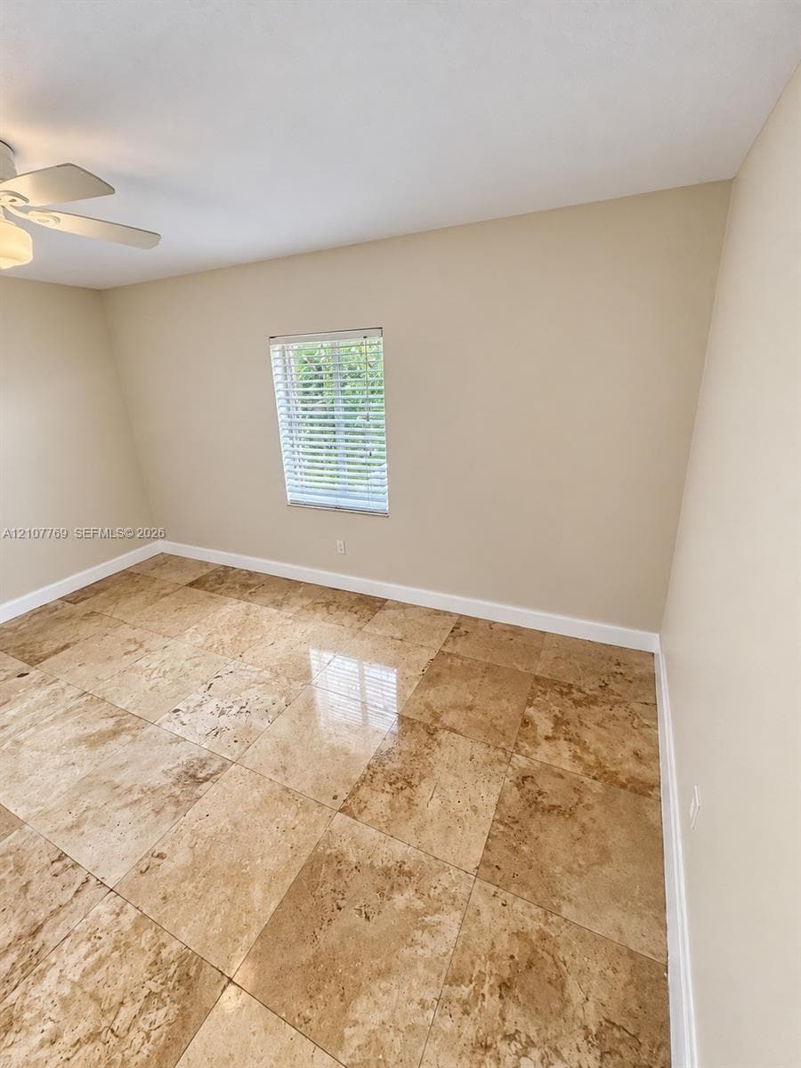 Neutral-toned interior space featuring polished stone tile flooring, a window with horizontal blinds, and a ceiling fan with integrated lighting