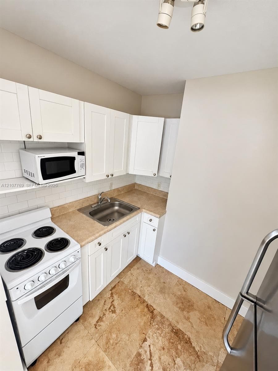 Kitchen featuring white cabinetry, stone-surface countertops, a subway tile backsplash, stainless steel sink, and natural stone flooring