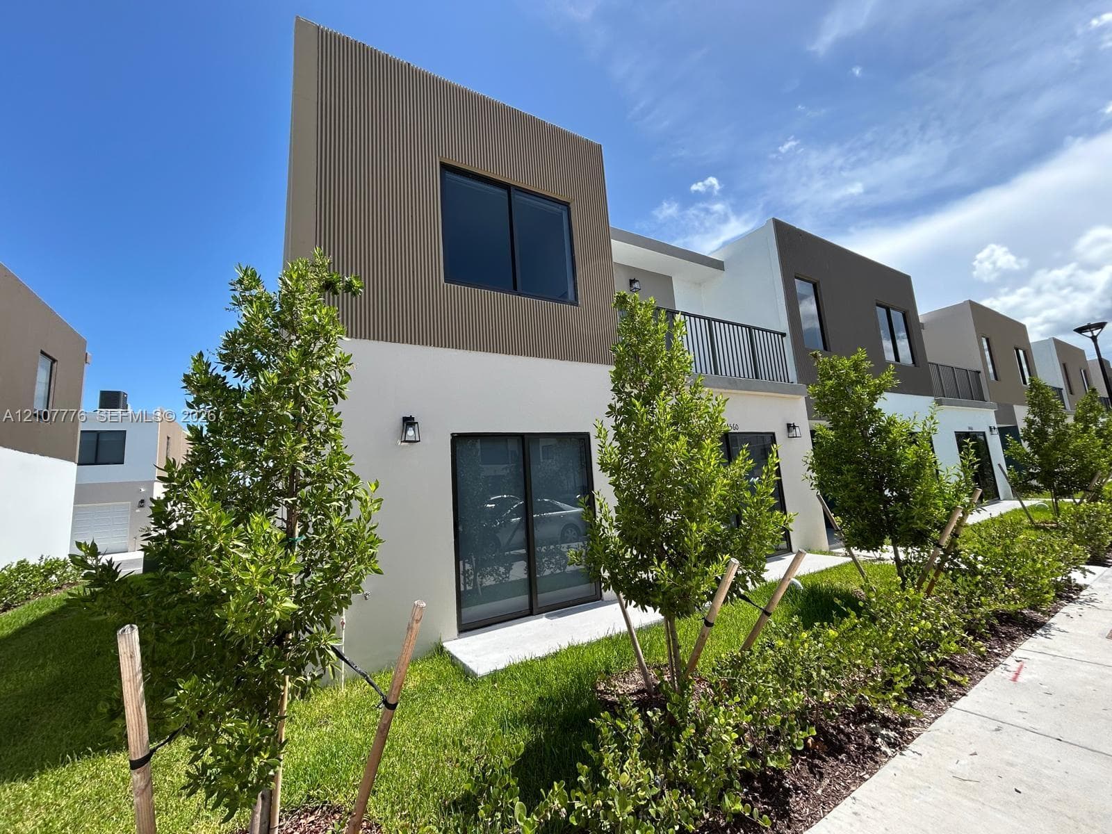 Modern two-story exterior featuring a smooth stucco finish, vertical ribbed siding, second-level metal balcony railings, sliding glass doors, and concrete patios