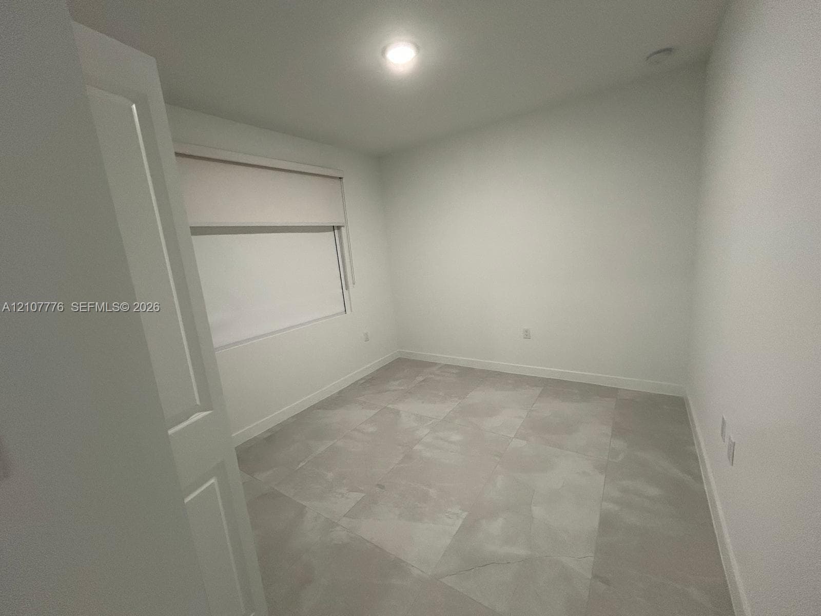 Neutral-toned room featuring large-format tile flooring, crisp white walls, and a recessed ceiling light fixture