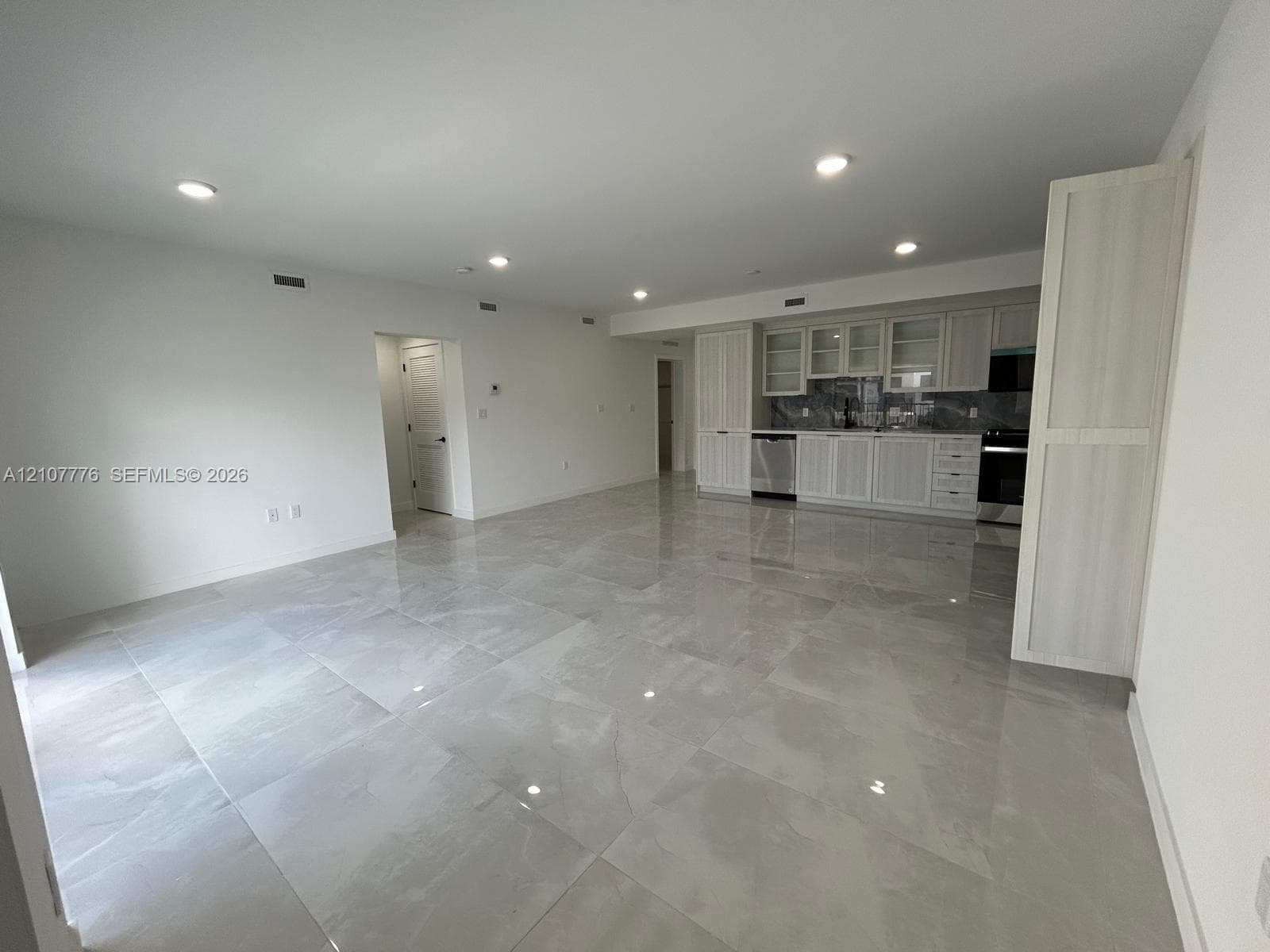 Large-format tile flooring, recessed ceiling lighting, light-toned cabinetry with glass-front uppers, and stainless-steel appliances