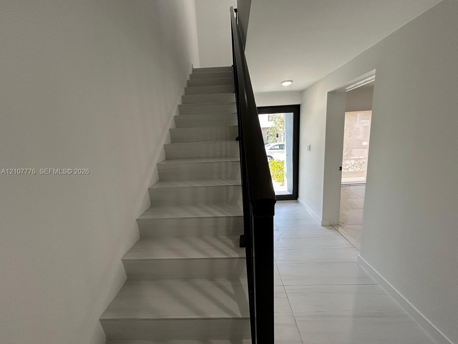 Staircase featuring white stone-finish steps and a black metal railing, complemented by large-format light-toned tile flooring and recessed ceiling lighting