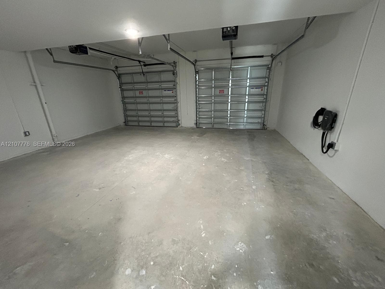 Two-car garage featuring dual sectional overhead doors, concrete flooring, and a wall-mounted electric vehicle charging station