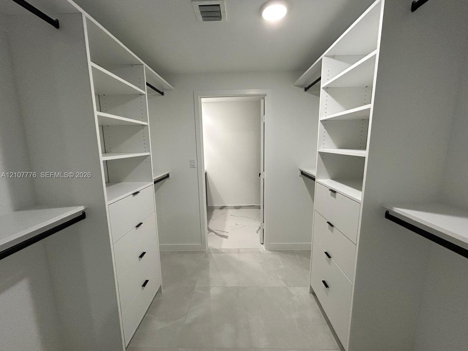 Walk-in closet featuring white built-in shelving, integrated dresser drawers with matte black hardware, and large-format tile flooring