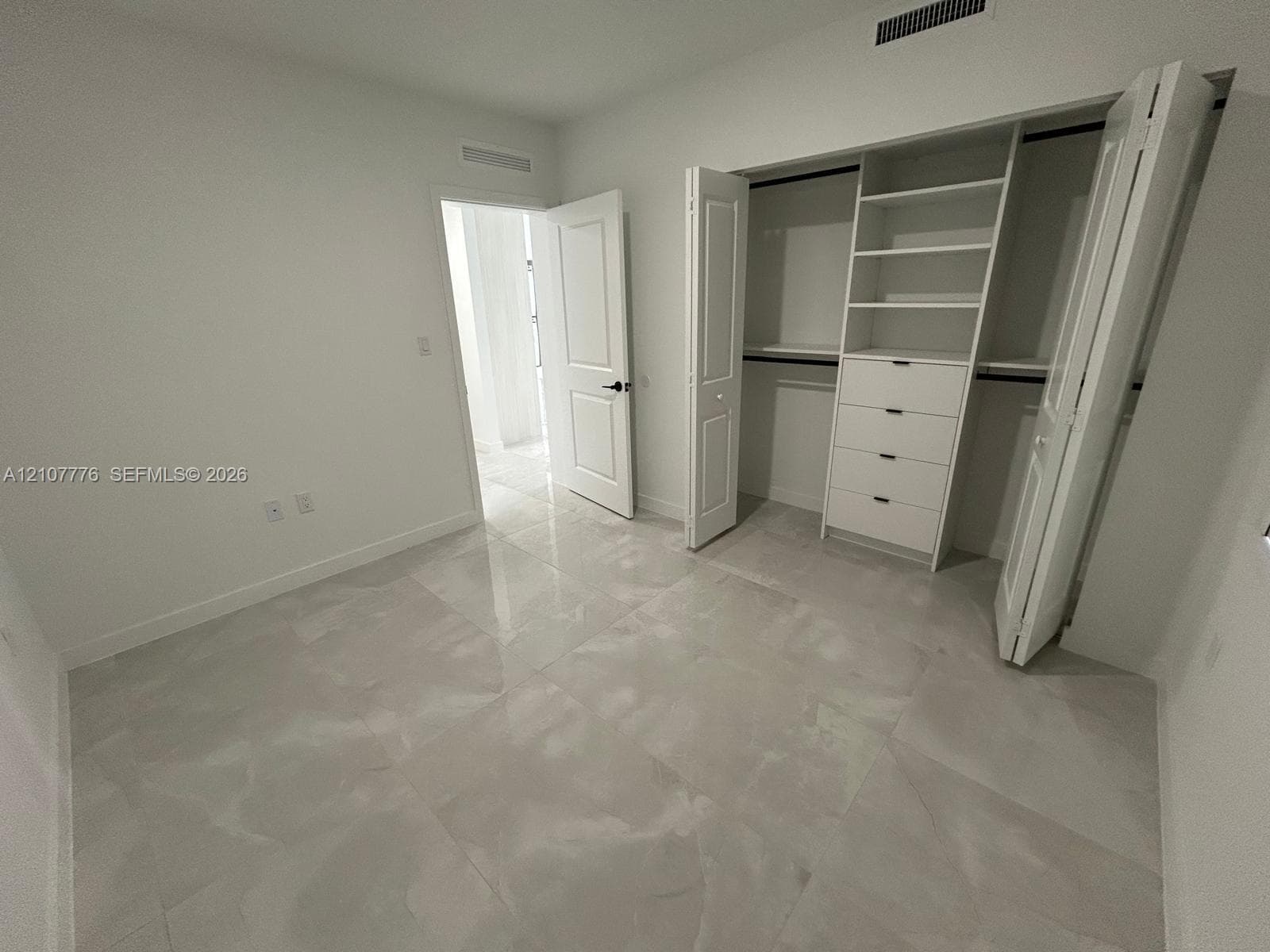 Room featuring large-format tile flooring, a custom walk-in closet with built-in shelving and drawers, and panel-style interior doors