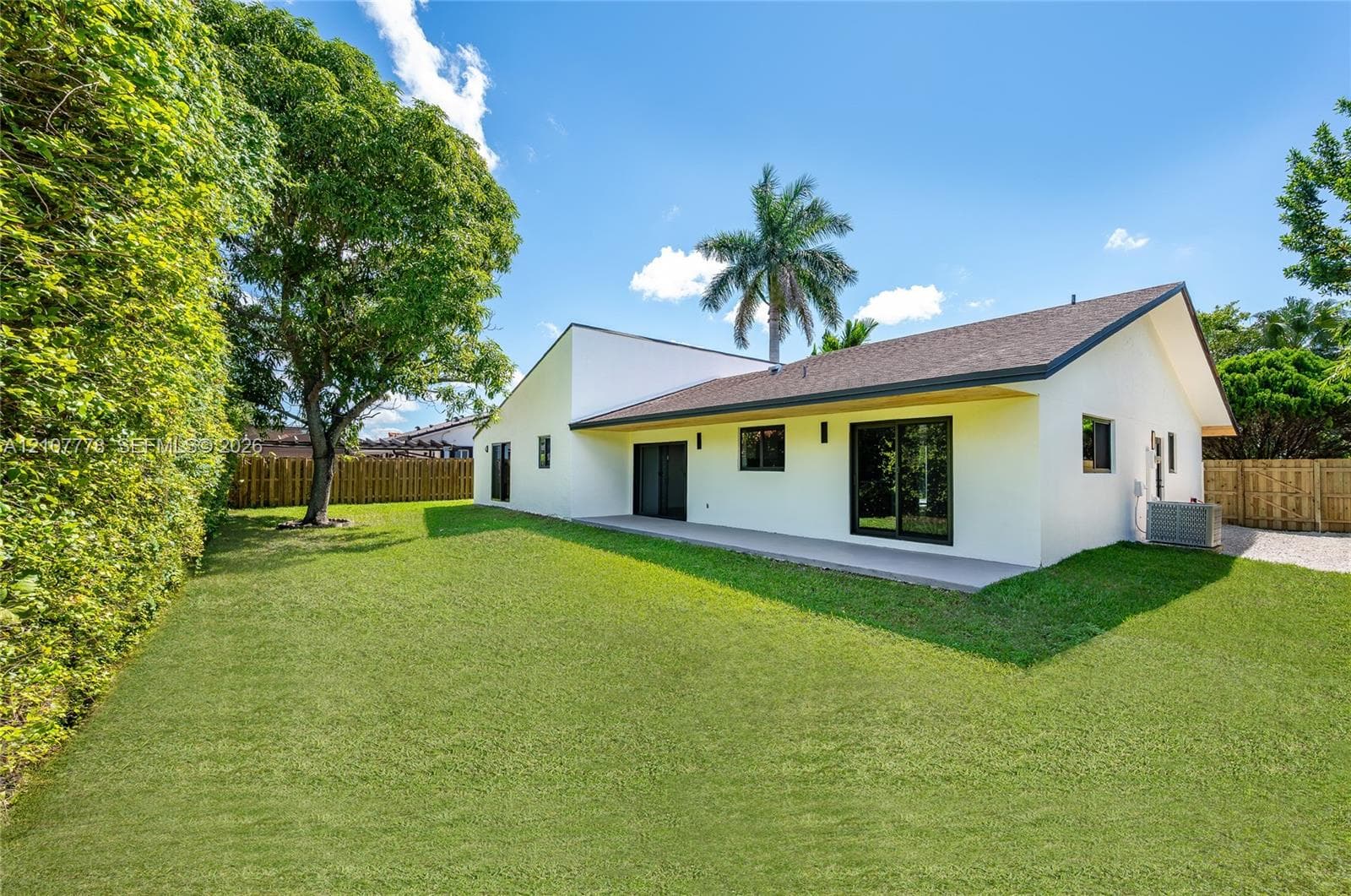 Exterior featuring a white stucco facade, expansive backyard lawn, concrete patio, sliding glass doors, and privacy fencing