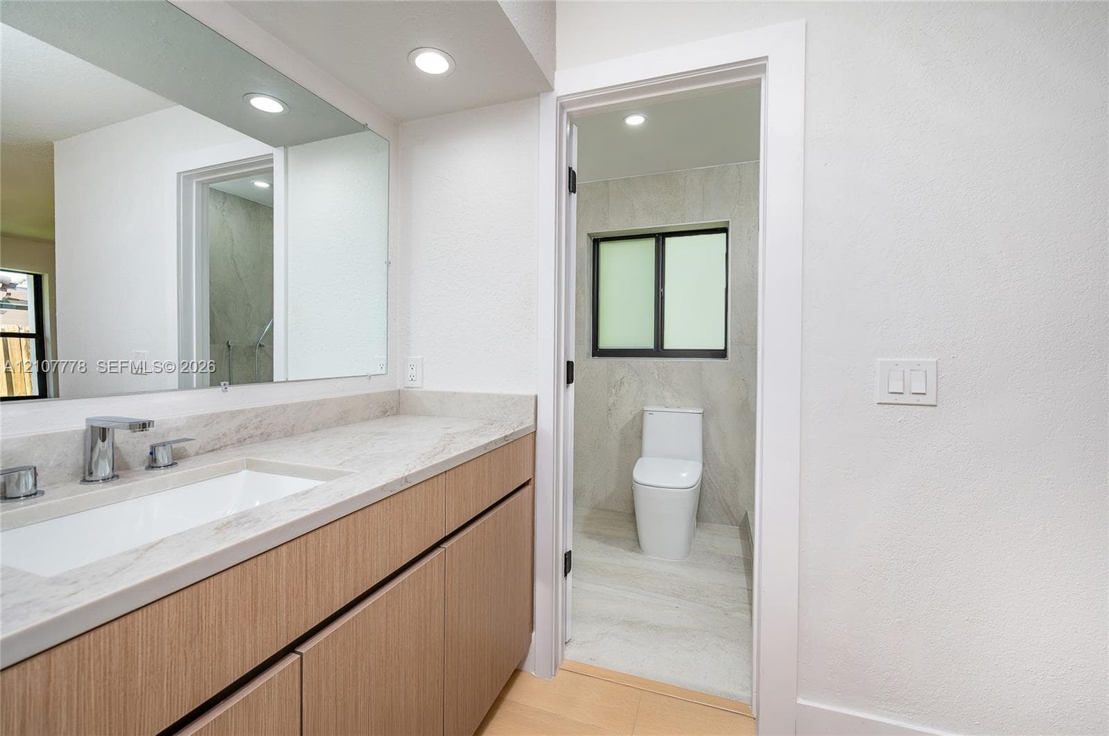 Bathroom featuring a wood-finish vanity with a stone-top integrated sink, a large wall-to-wall mirror, recessed lighting, and tile flooring
