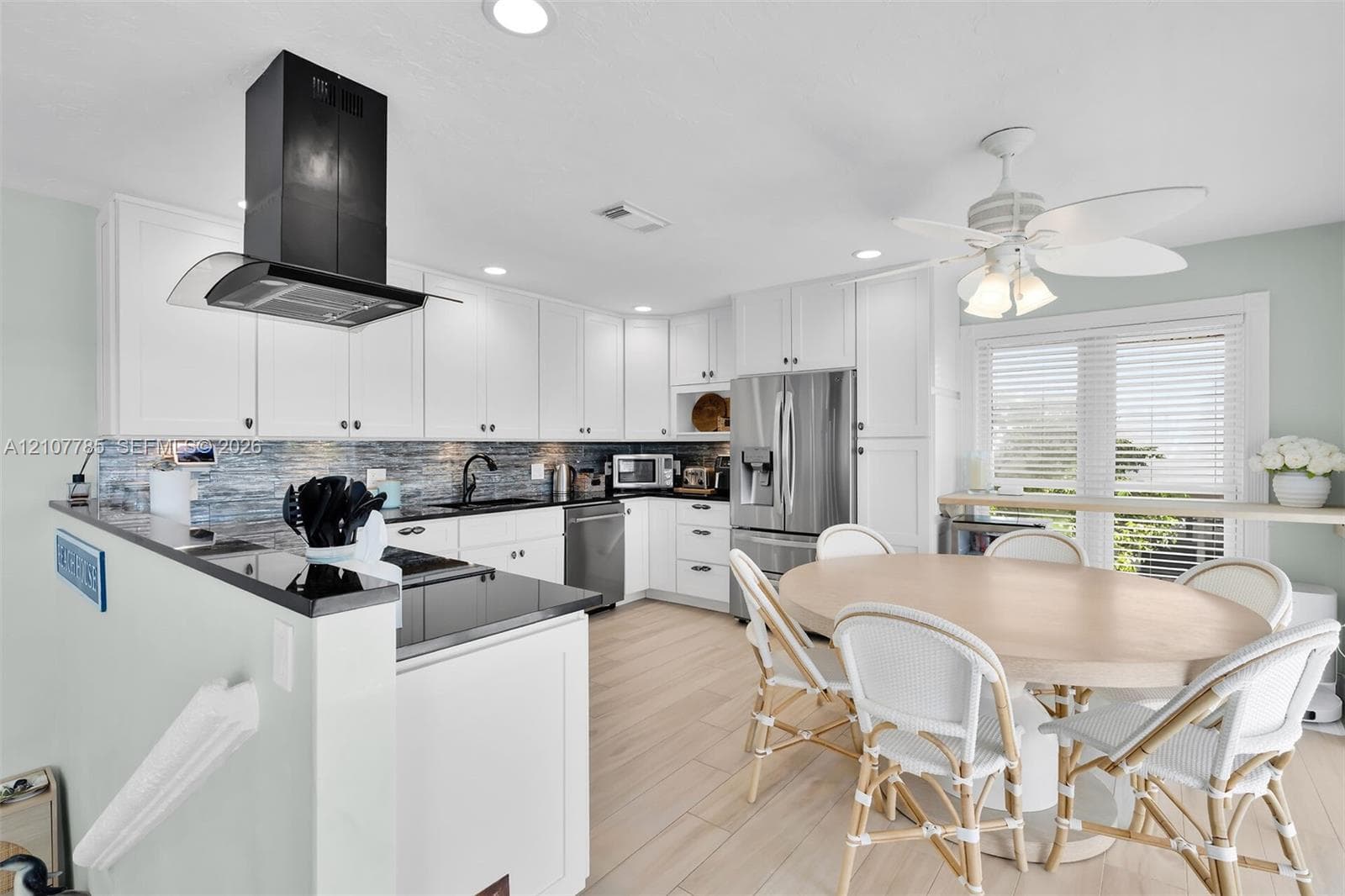 Kitchen featuring white shaker-style cabinetry, dark stone countertops, a stainless steel refrigerator, a black wall-mounted range hood, and wood-finish flooring