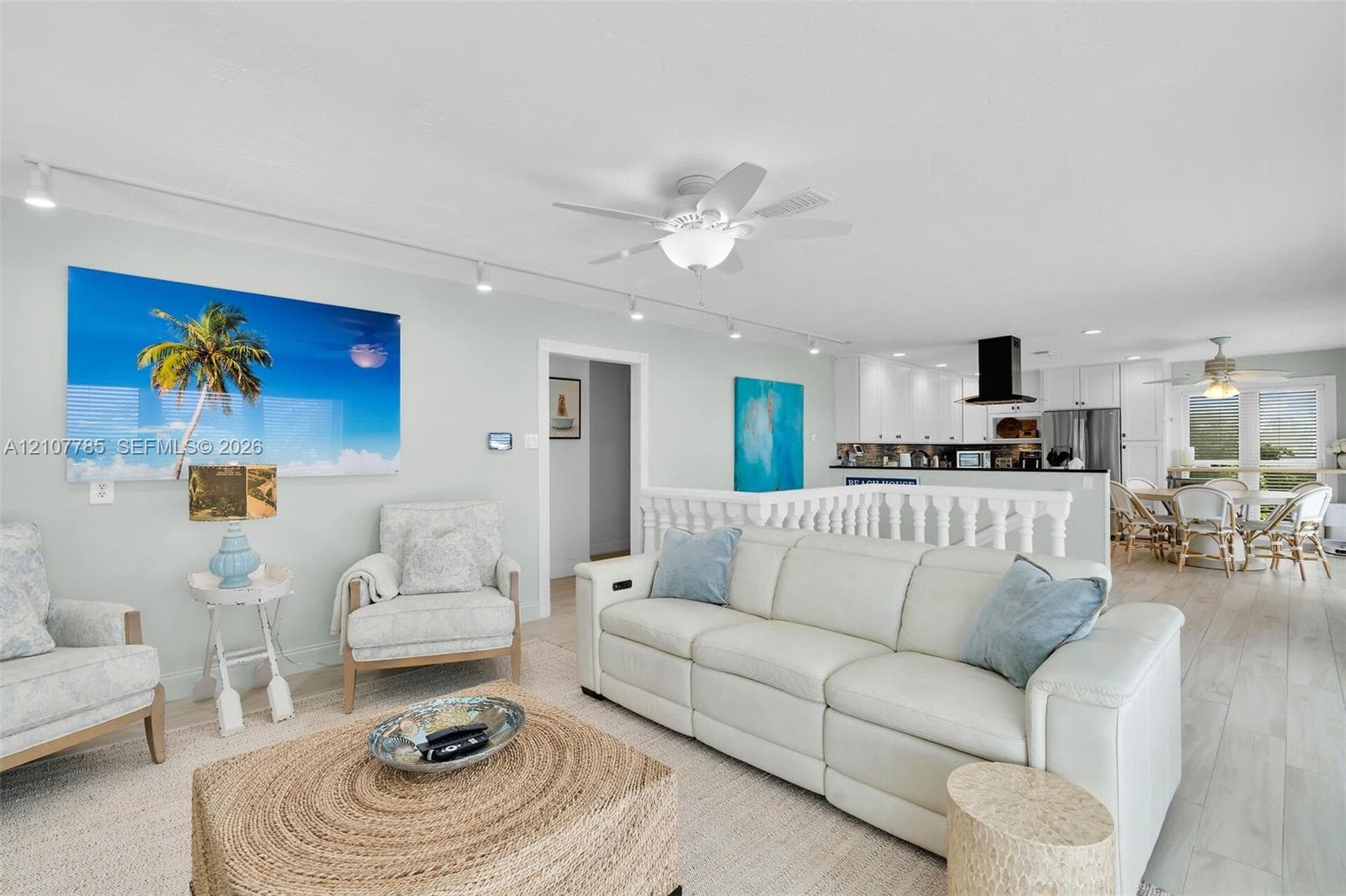 Open-concept interior featuring wood-finish flooring, white cabinetry, track lighting, ceiling fans, and balustrade railing