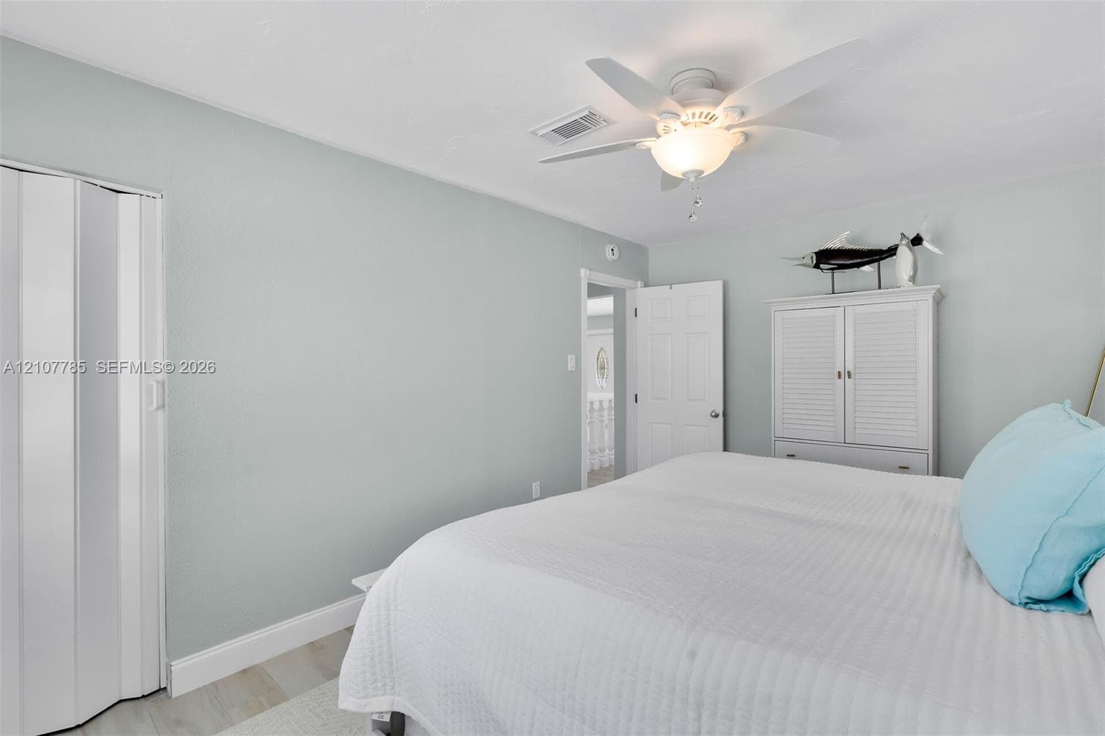 Light-toned wood-finish flooring, white bifold closet doors, six-panel interior door, and a ceiling fan with integrated light fixture