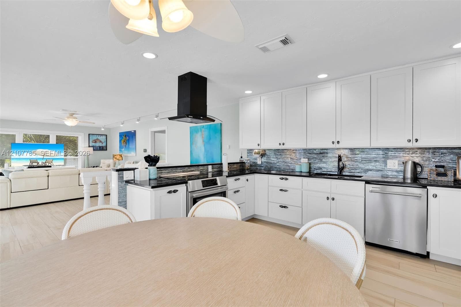 Kitchen featuring white cabinetry, dark countertops, a textured tile backsplash, a stainless steel dishwasher, and a matte black wall-mounted range hood