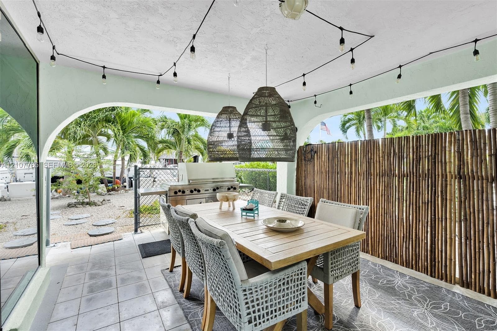 Covered patio featuring ceramic tile flooring, built-in stainless steel outdoor kitchen, arched architectural detailing, and decorative woven pendant lighting