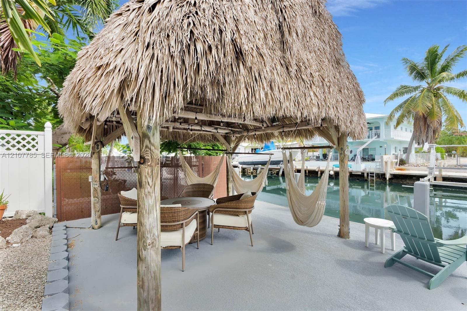 Thatch-roofed gazebo featuring timber support posts, concrete hardscaping, and direct water access with a concrete bulkhead