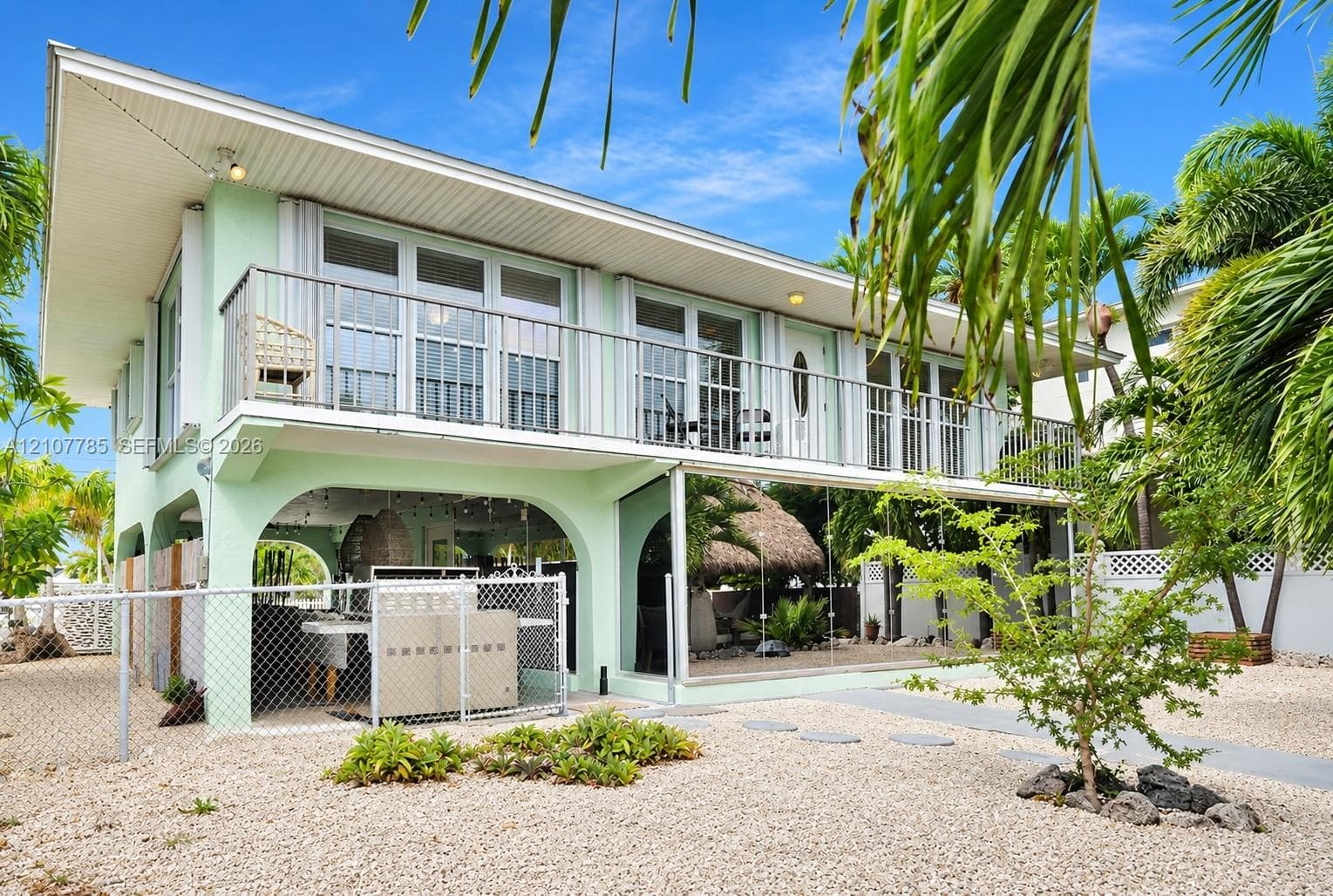 Elevated exterior featuring a second-story balcony with metal railing, ground-level covered patio with arched masonry, and exterior staircase