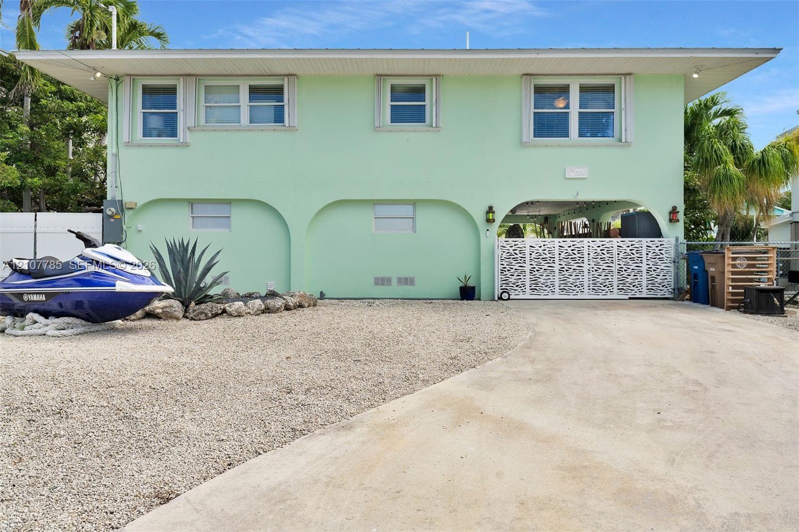 Two-story residence featuring architectural arched structural supports, a decorative metal privacy gate, concrete driveway, and low-maintenance gravel landscaping