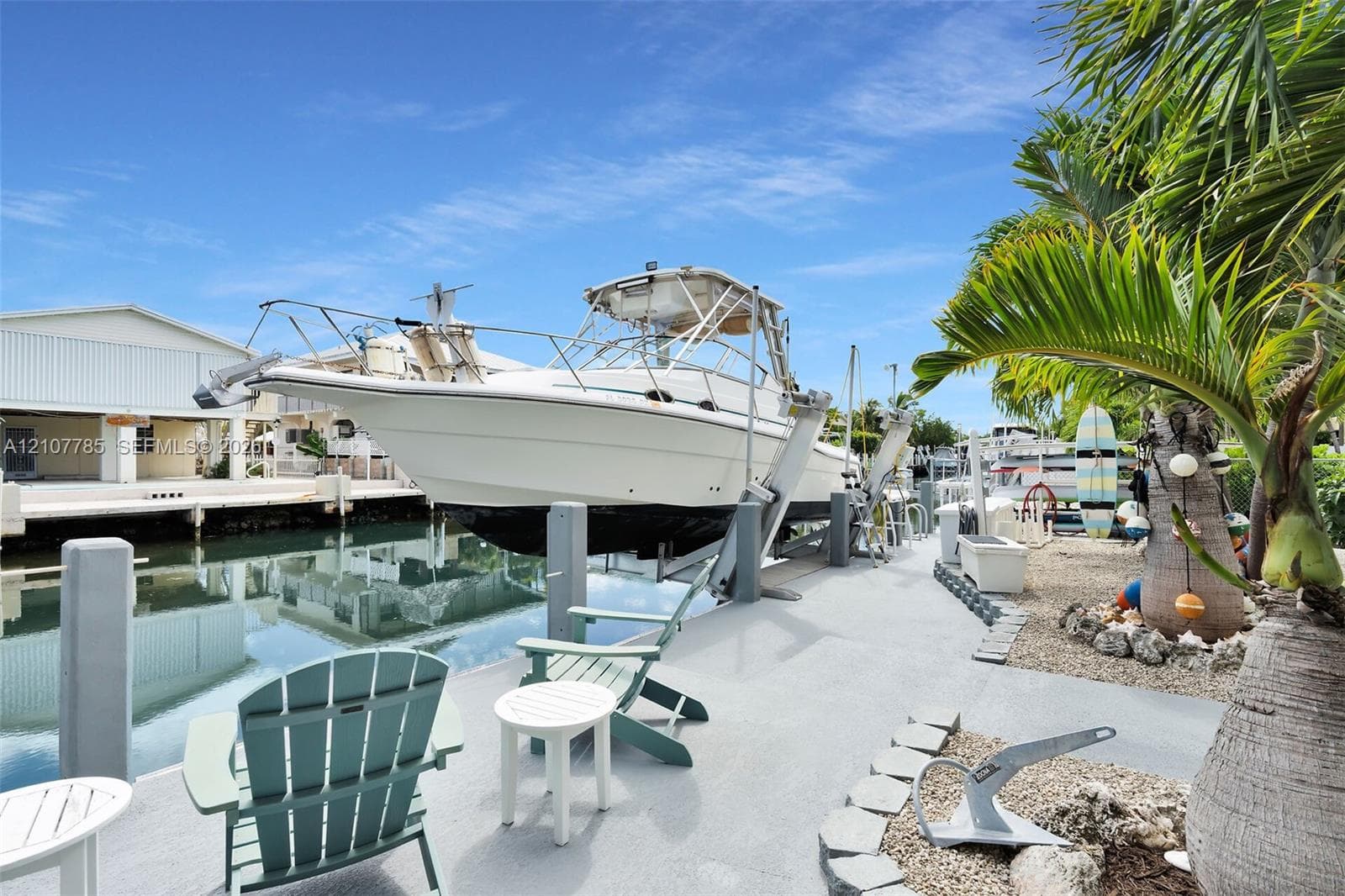 Waterfront canal property featuring a private boat lift, concrete bulkhead, graveled landscaping, and mature palm trees