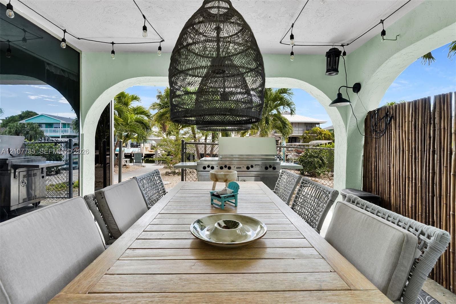 Covered outdoor living space featuring arched structural openings, built-in stainless steel grill, woven pendant light fixture, and mounted exterior wall sconces
