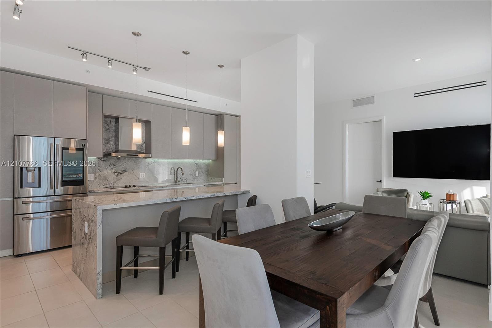 Modern kitchen featuring flat-panel cabinetry, stone-finish countertops with a waterfall edge, stainless steel appliances, and pendant lighting