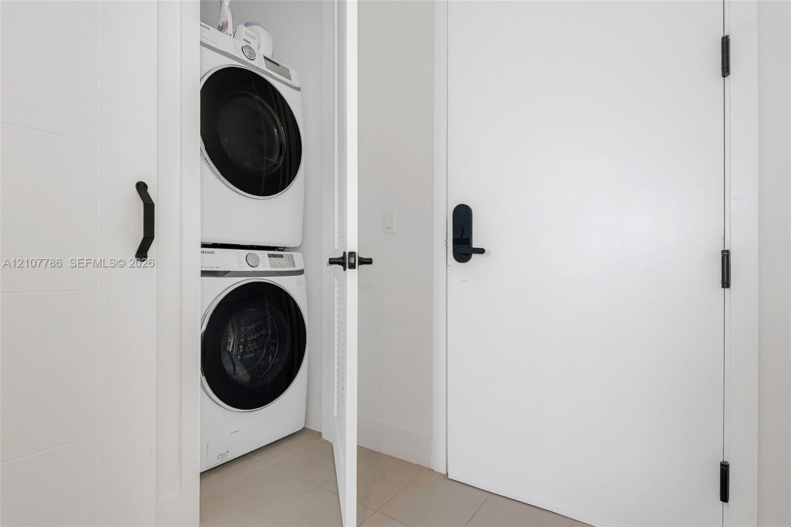 Laundry closet featuring a stacked white front-load washer and dryer, matte black hardware, and louvered door detailing