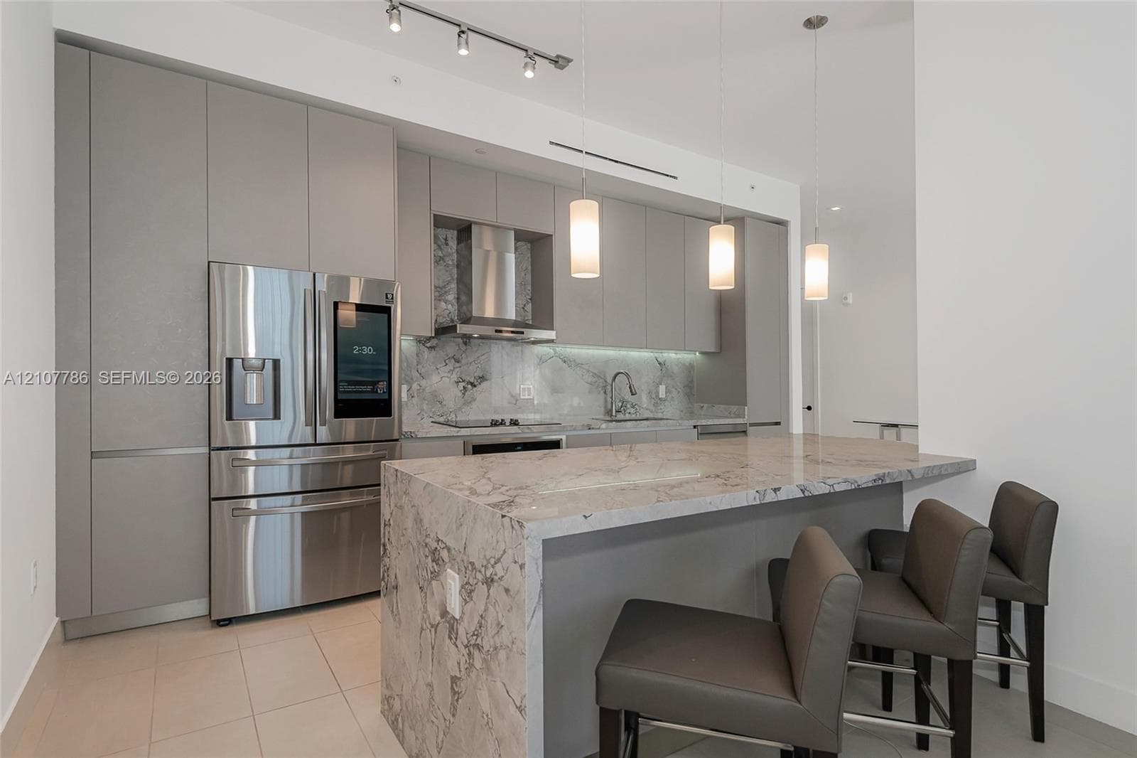 Contemporary kitchen featuring flat-panel cabinetry, stone countertops with waterfall edge, stainless steel appliances, integrated range hood, and pendant lighting