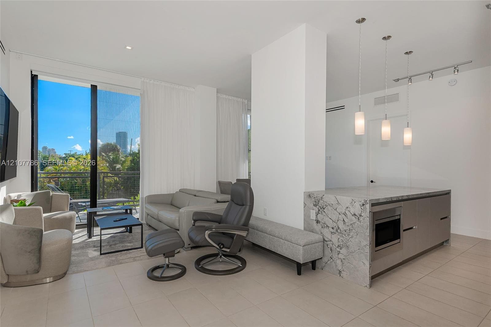 Open-concept floor plan featuring tile flooring, stone-surfaced kitchen island with integrated cabinetry, floor-to-ceiling glass paneling, and three cylindrical pendant light fixtures