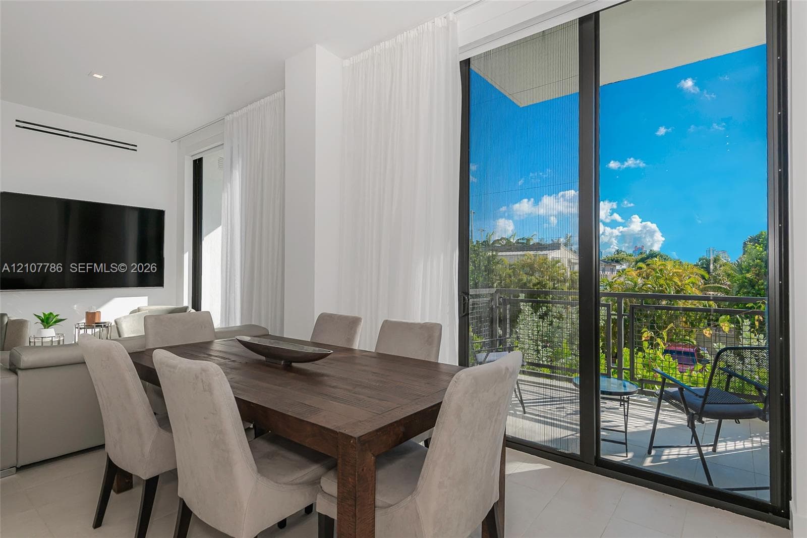 Floor-to-ceiling sliding glass doors, private balcony with metal railing, neutral tile flooring, and recessed ceiling lighting