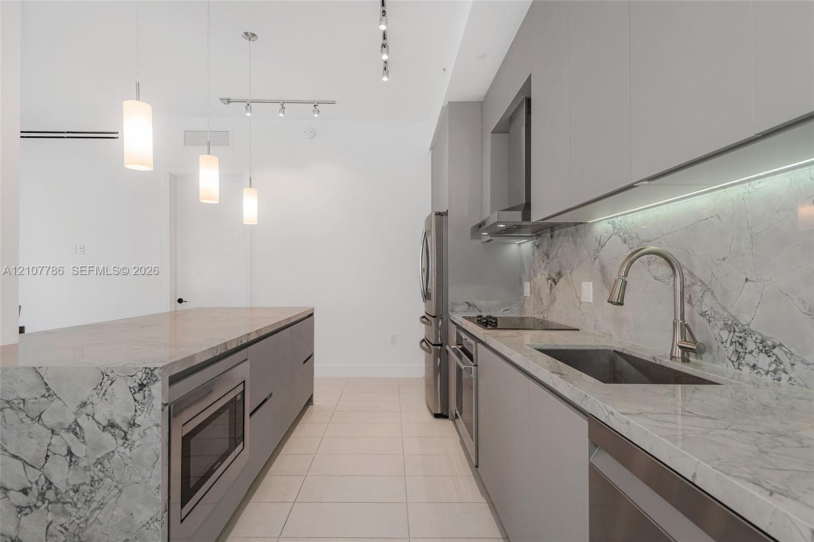 Contemporary kitchen featuring a waterfall island, stone countertops, integrated stainless steel appliances, flat-panel cabinetry, and under-cabinet lighting