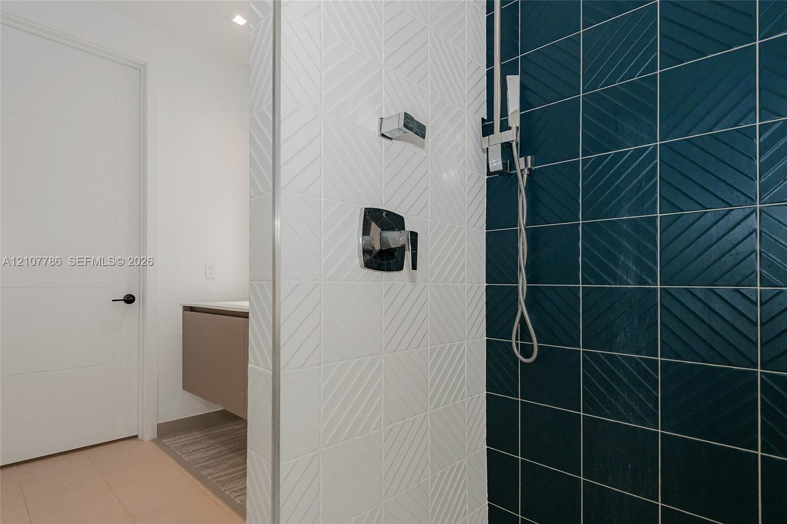 Walk-in shower featuring textured white and deep blue square wall tiles, chrome hardware, handheld showerhead, and a floating vanity