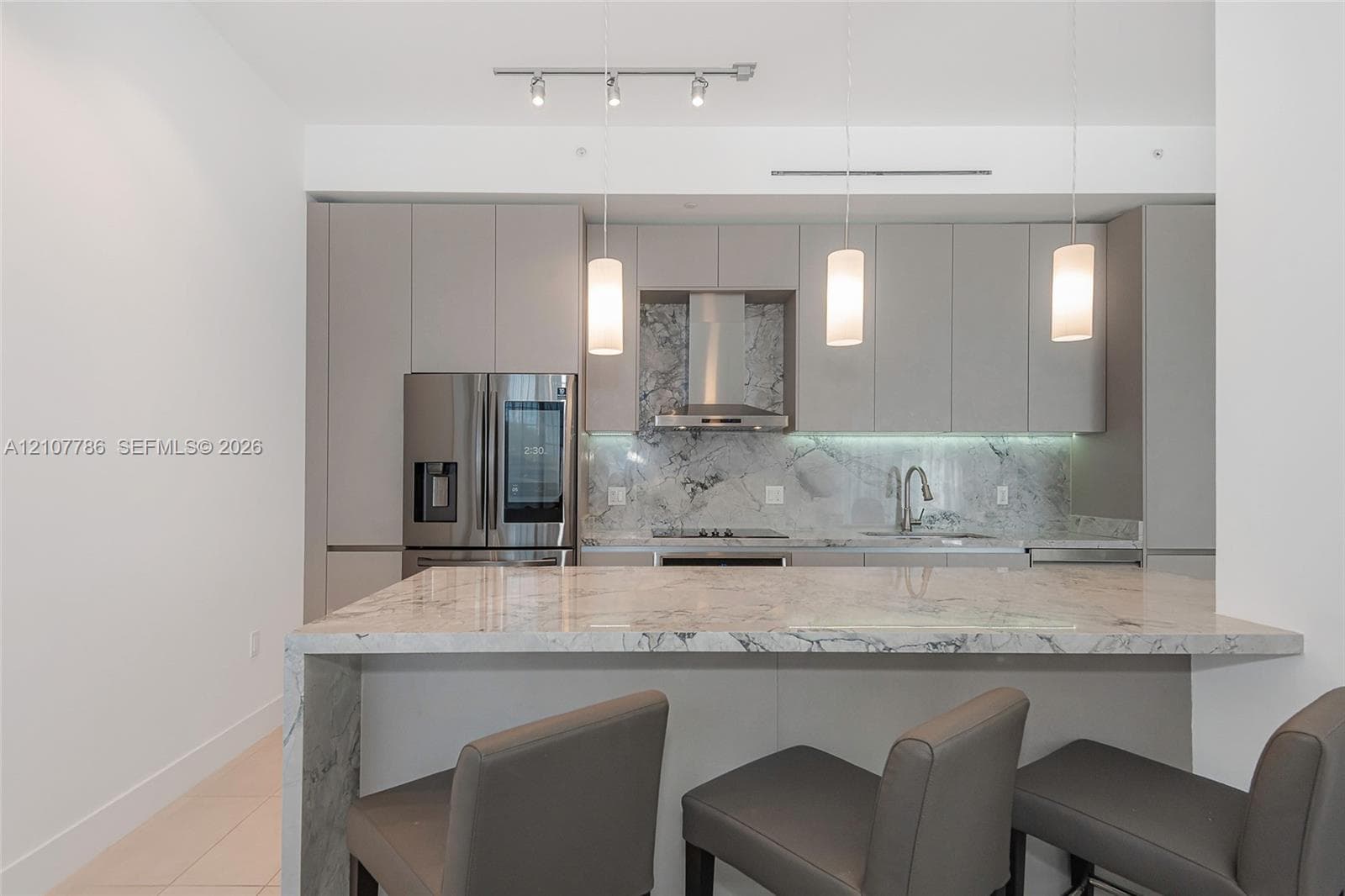 Kitchen featuring waterfall island with stone countertop, stainless steel appliances, flat-panel cabinetry, stone backsplash, and pendant lighting