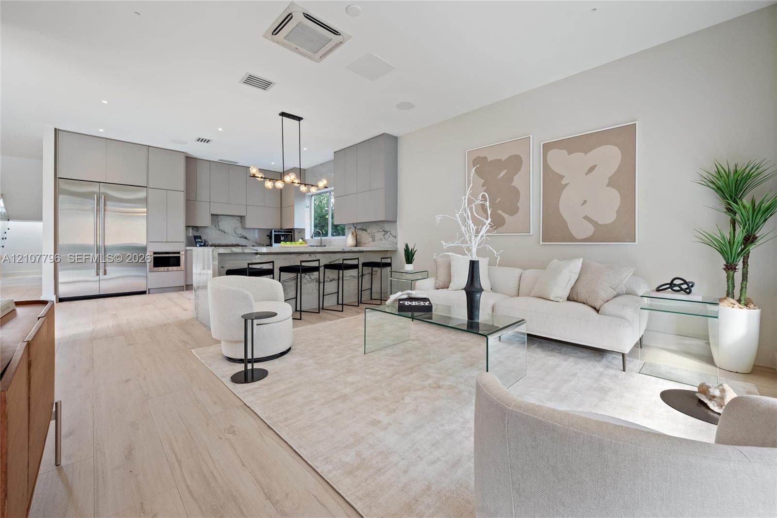 Modern kitchen and living area featuring wood-finish flooring, floor-to-ceiling cabinetry, a stone-surfaced waterfall edge island, and a multi-globe pendant light fixture