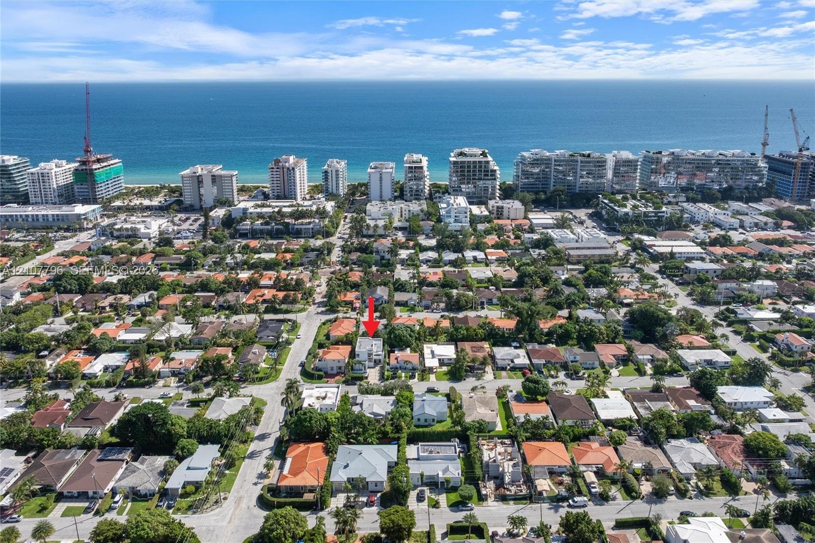 Aerial perspective of a residential property featuring dense perimeter landscaping and mature trees, located within a coastal neighborhood