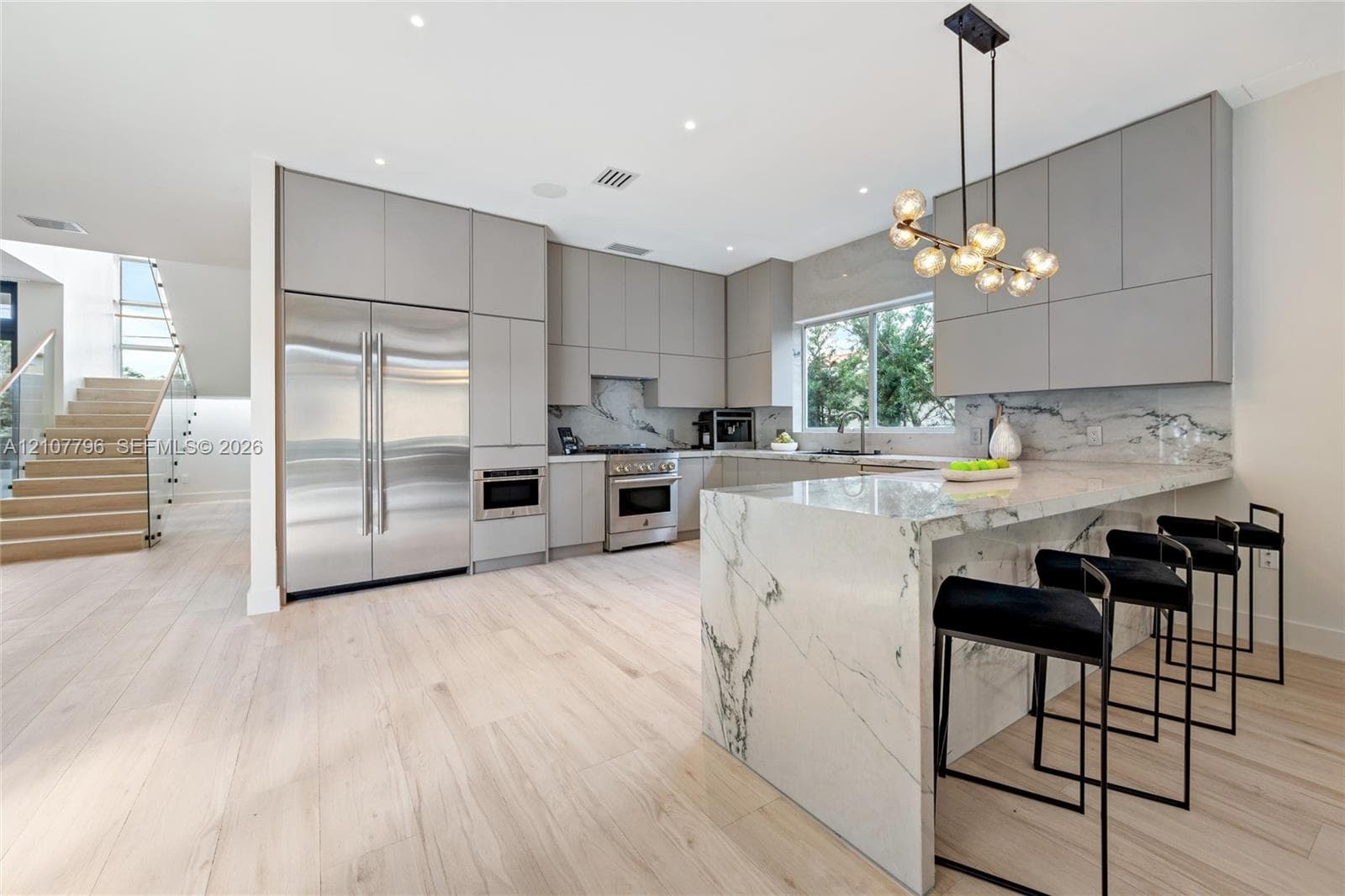 Modern kitchen featuring flat-panel cabinetry, waterfall-edge stone island, stainless steel appliances, and stone slab backsplash