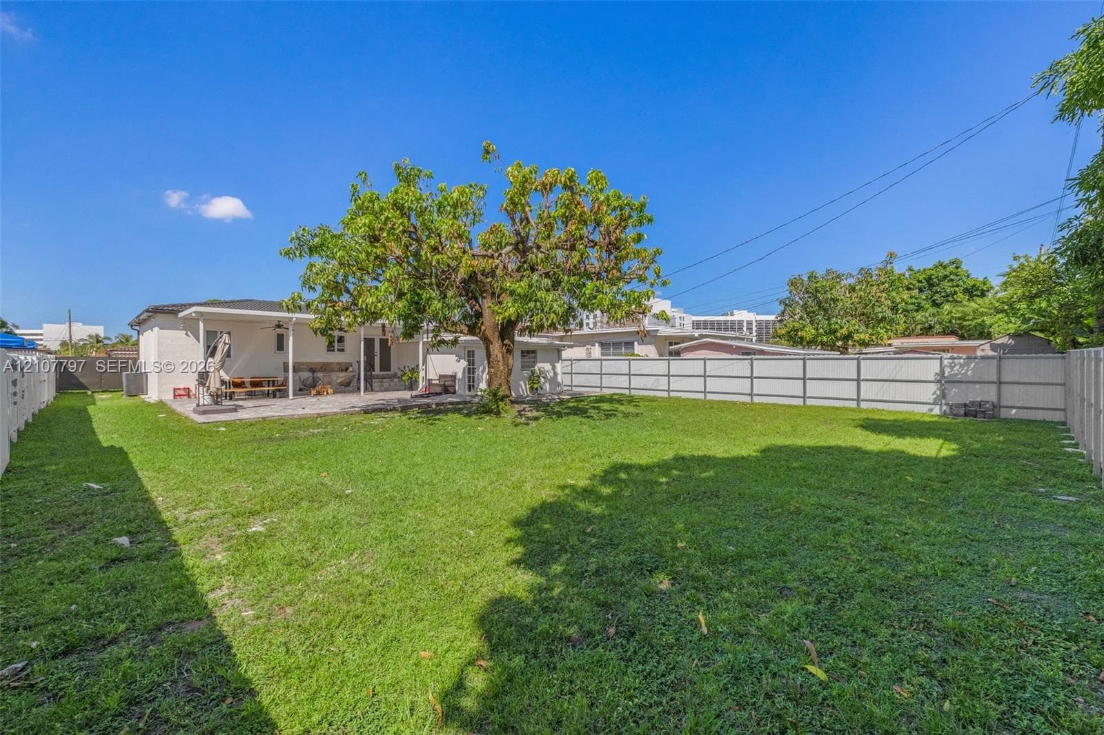 Expansive backyard featuring a central mature tree, paved patio area, and full-perimeter vinyl fencing