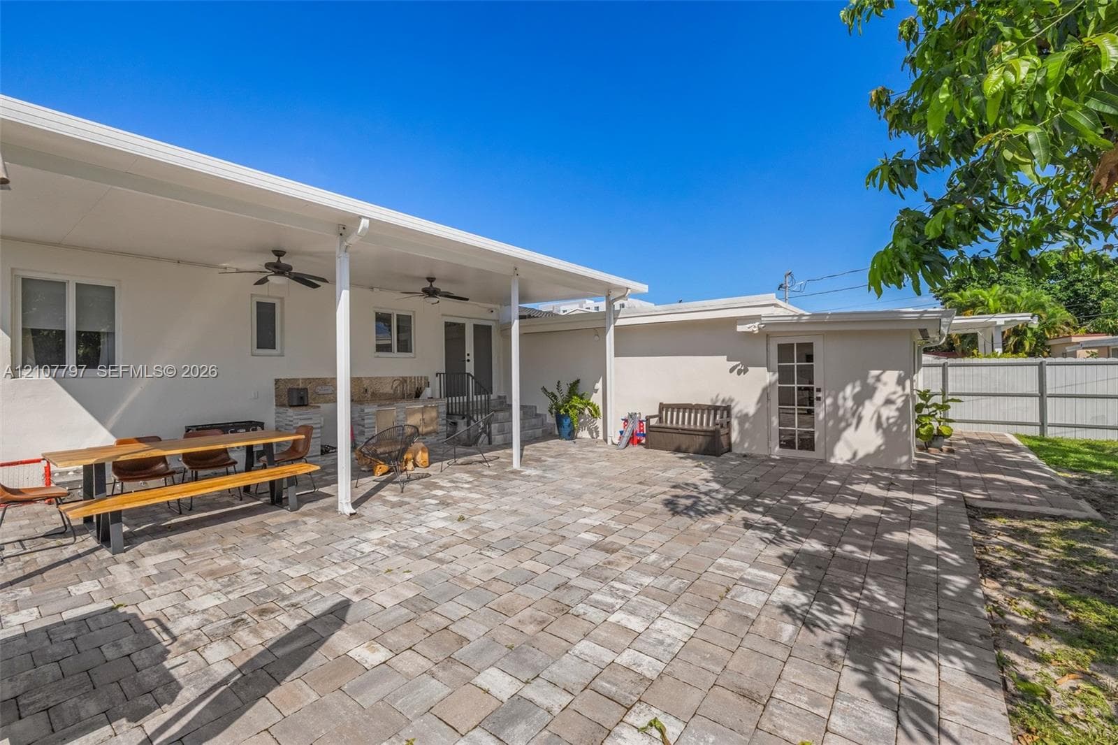 Expansive backyard featuring a large grass lawn, a covered concrete patio, a mature shade tree, and perimeter fencing