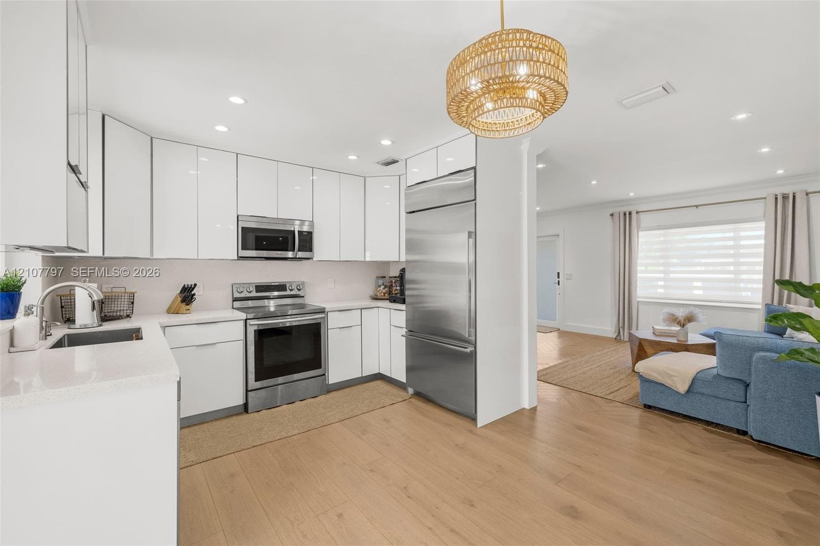 Kitchen featuring gloss-finish cabinetry, stainless steel appliances, light-toned stone countertops, wood-finish flooring, and a textured pendant light fixture