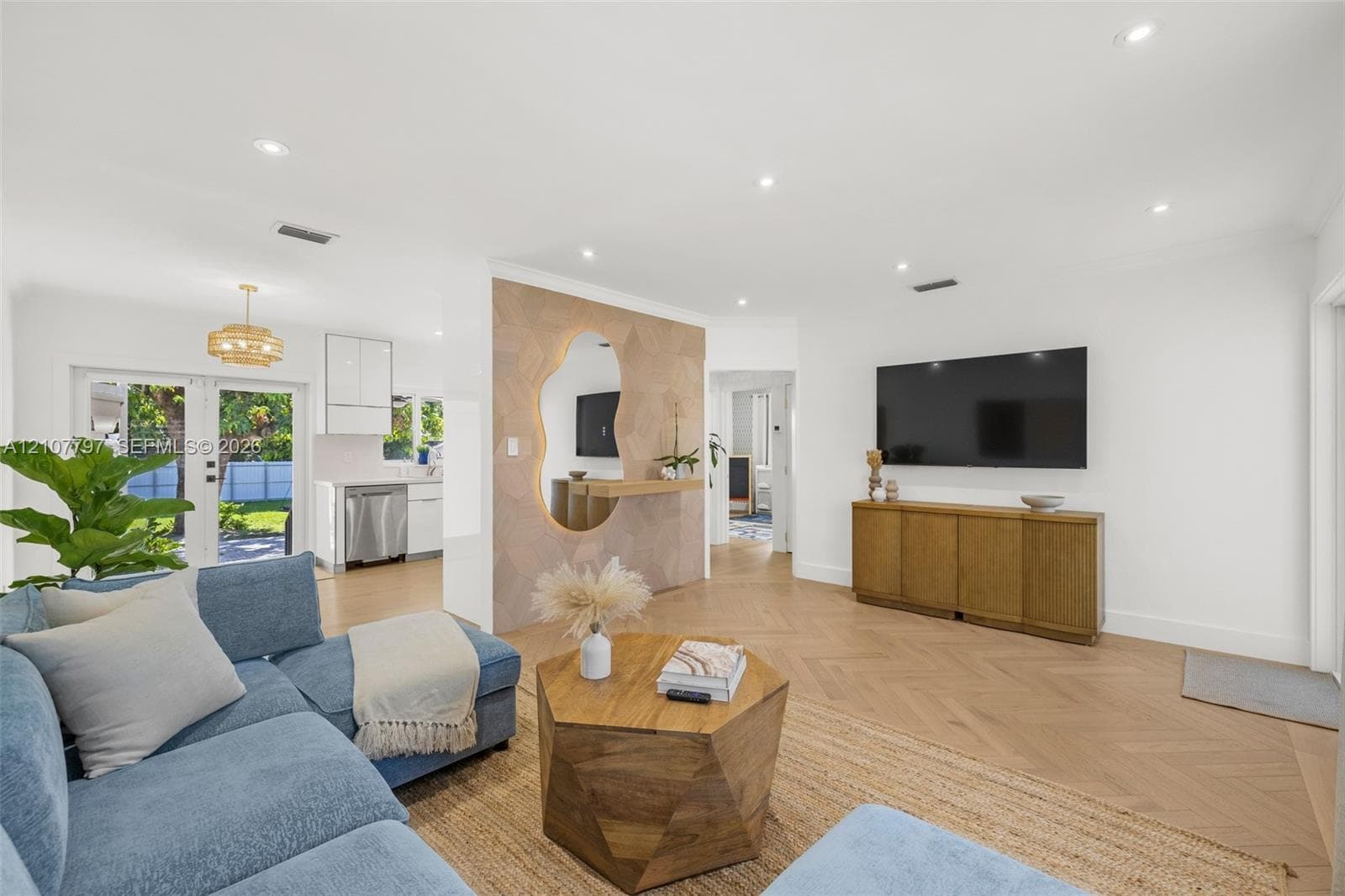 Open concept interior featuring herringbone-patterned wood-finish flooring, recessed lighting, and a textured accent wall with a geometric backlit mirror