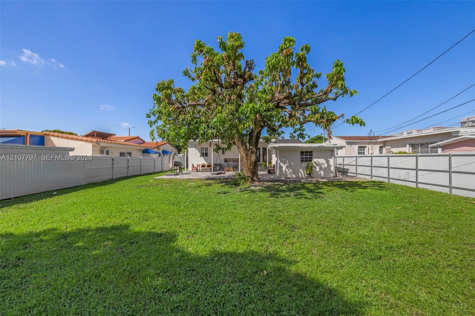 Expansive backyard featuring a large central tree, perimeter vinyl fencing, and a concrete patio