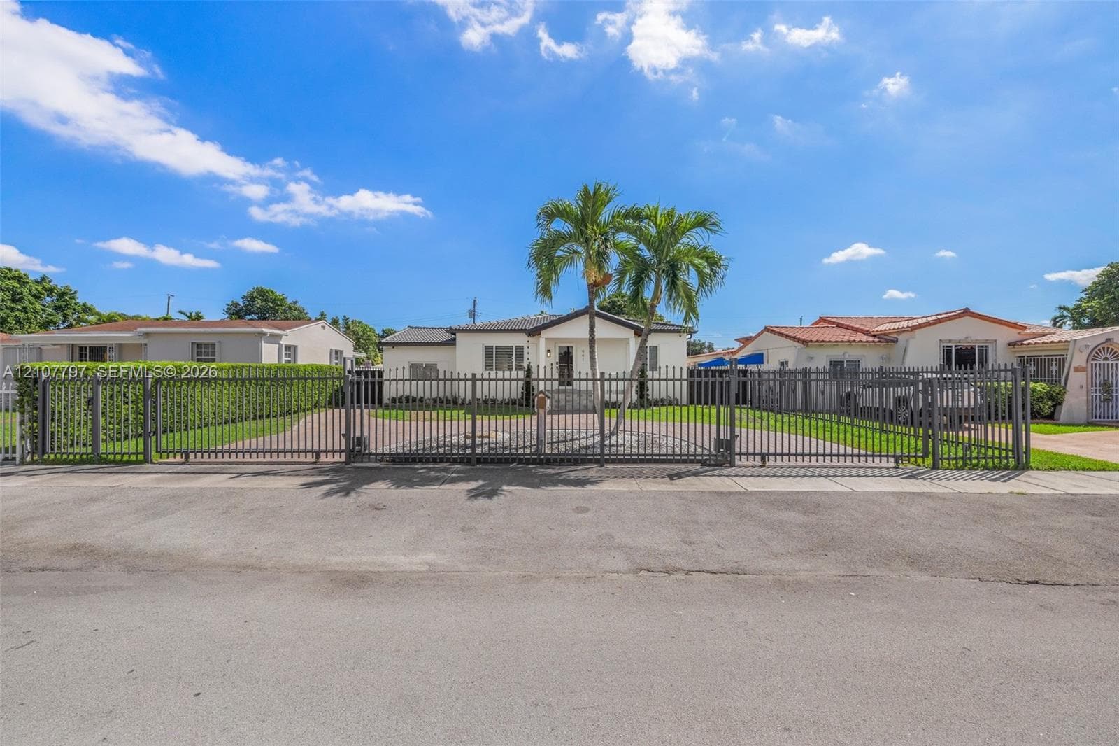 Single-story residence featuring a paved brick driveway, covered entryway with stone steps, glass-panel railing, and metal perimeter fencing