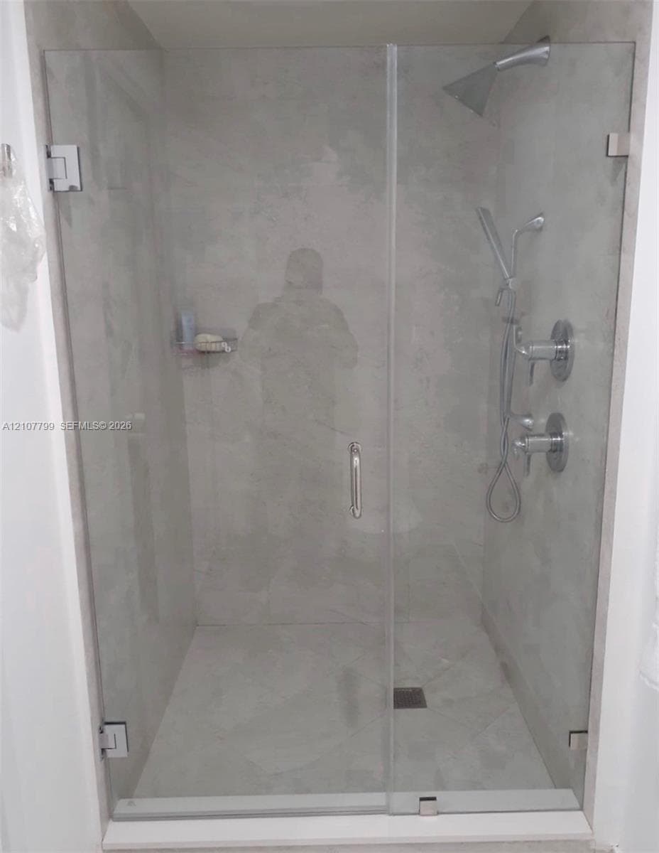 Walk-in shower featuring a frameless glass door, large-format tile surround, dual-head polished chrome shower system, and built-in corner shelving