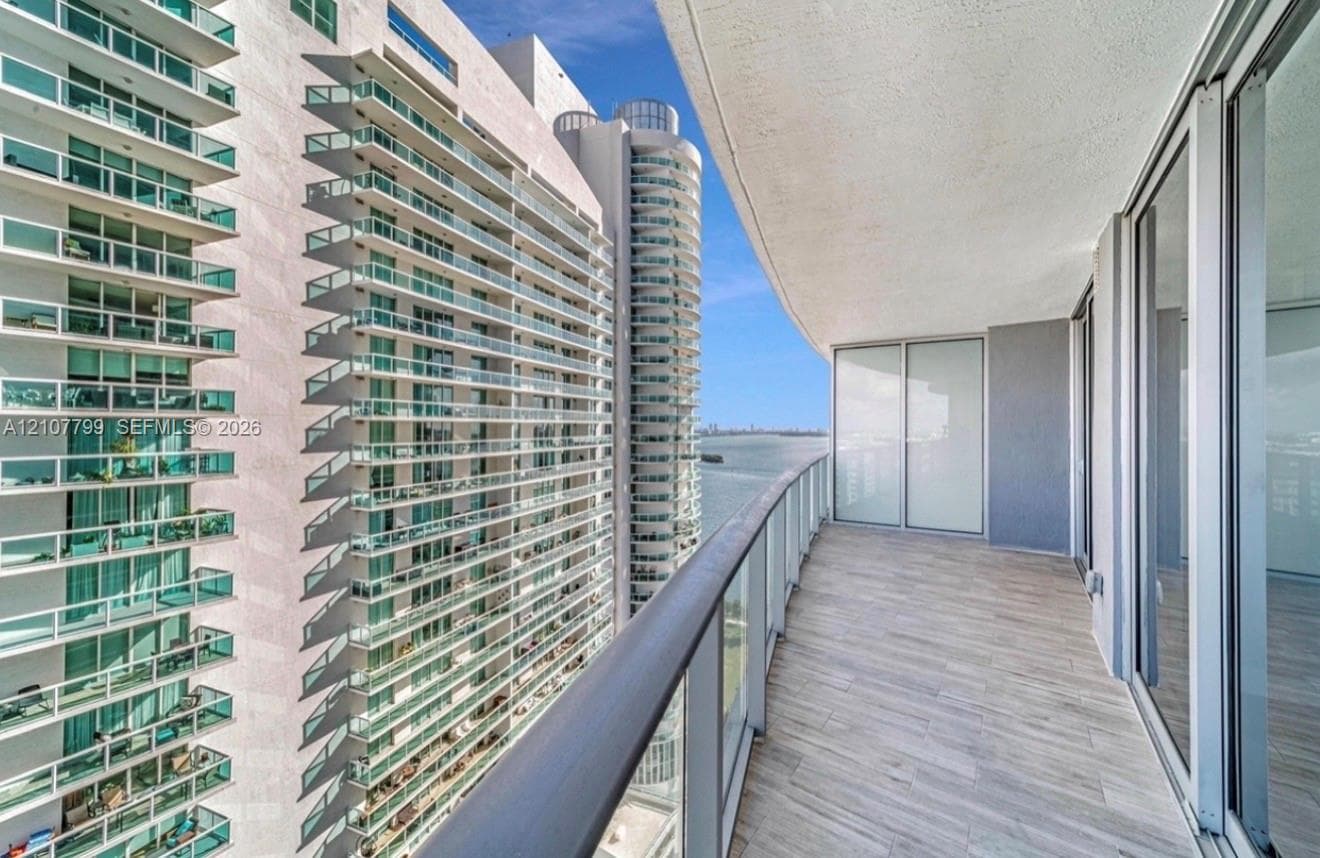 Covered balcony featuring wood-finish flooring, glass panel railing, and full-height sliding glass doors